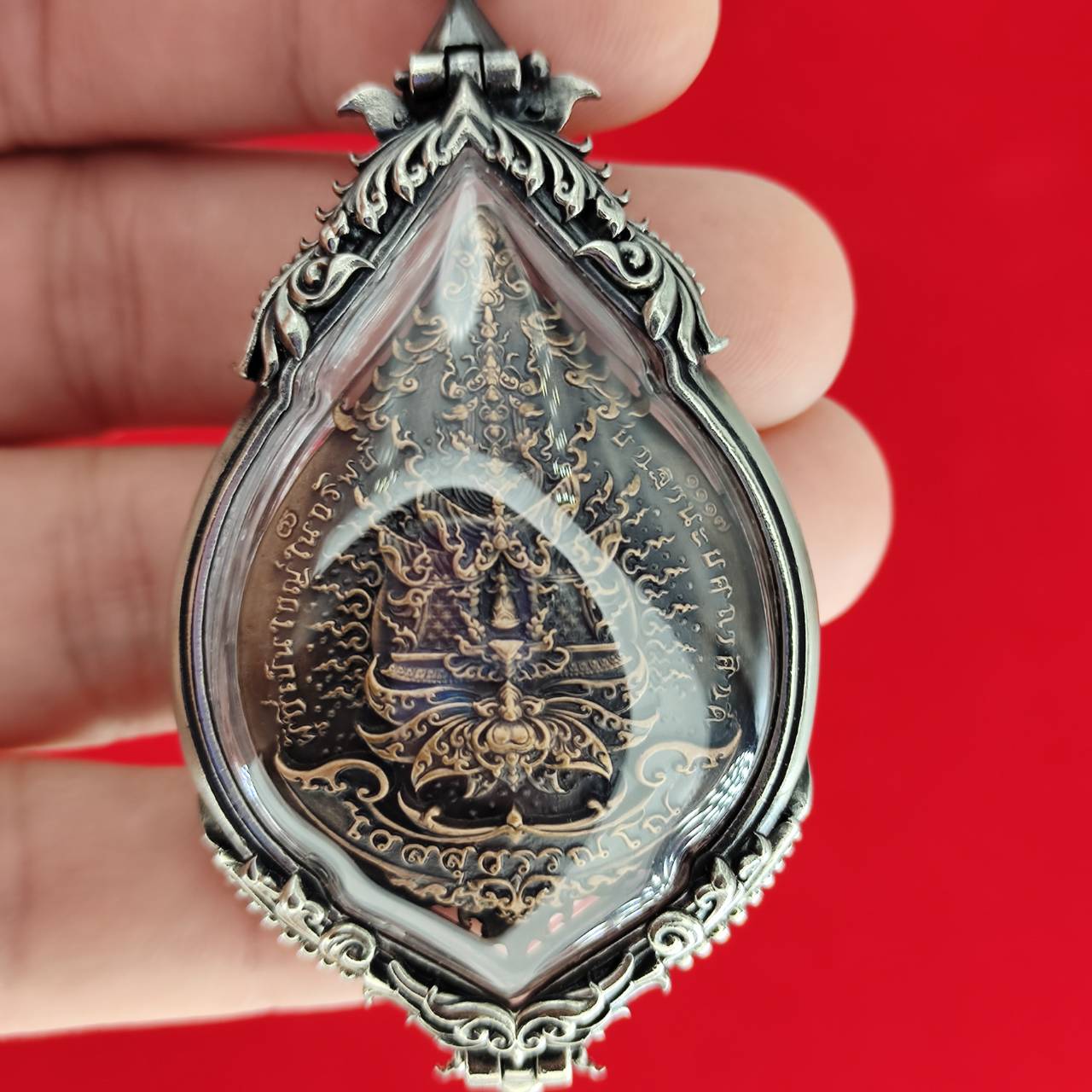 Silver teardrop amulet with Thai script and deity carving in resin case Lord Vesuvananno amulet for wealth and protection.