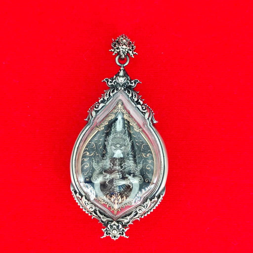 Thai Blessing Co ornate silver teardrop pendant featuring Lord Vesuvananno amulet for wealth and protection. Red fabric background
