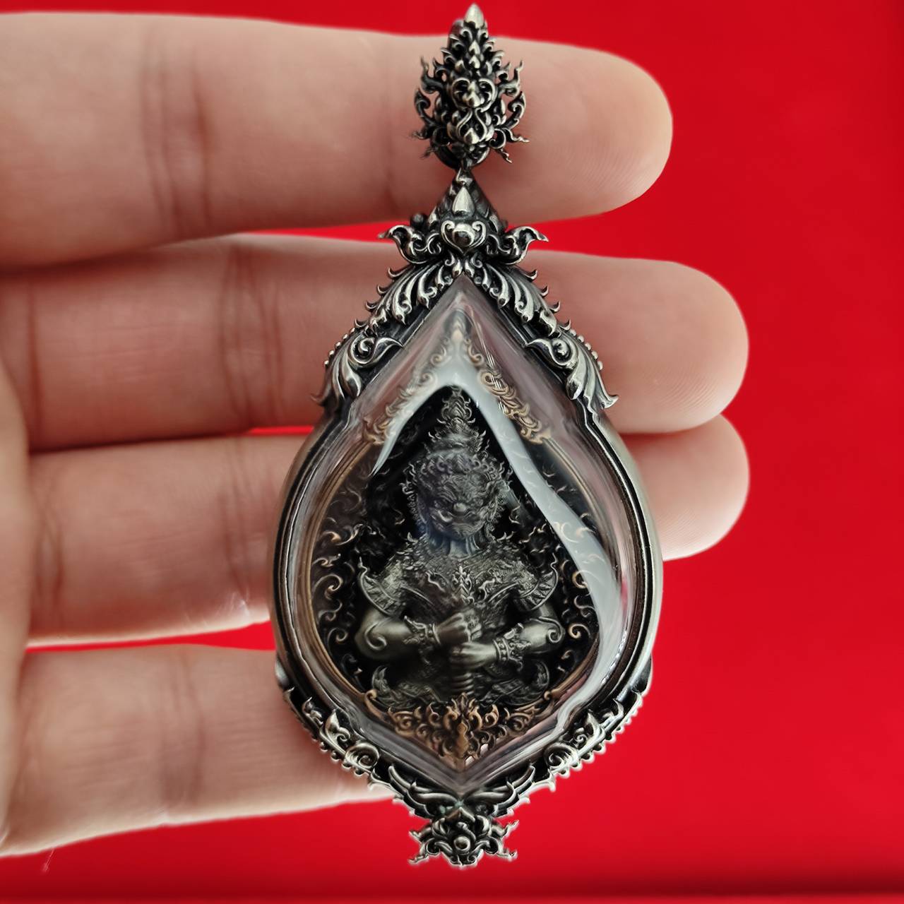 Lord Vesuvananno amulet for wealth and protection. Ornate Thai silver framed amulet held in hand against red background