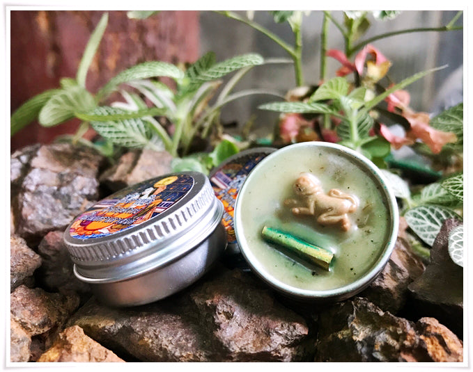 Thai attraction charm balm in a metal tin with a green base and decorative elements on rocks