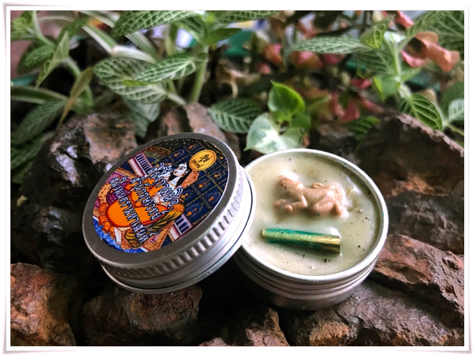 Thai attraction charm balm in a silver tin with intricate label design, placed on natural stone background