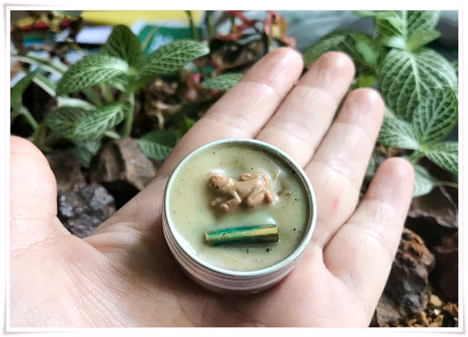 Hand holding Thai attraction charm balm with a figurine and herbal ingredients for attraction and positivity