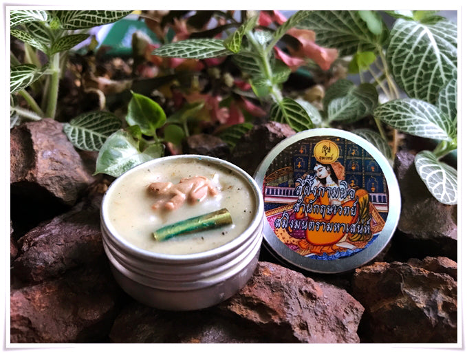 Thai attraction charm balm in a silver tin with herbal ingredients displayed among rocks and greenery