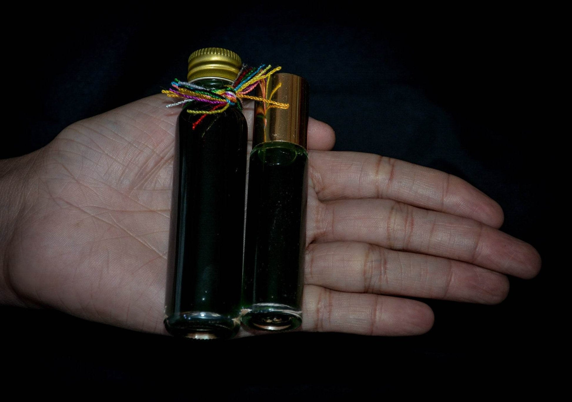 Two small dark glass bottles of Thai attraction oil for charisma held in a person’s hand against a black background