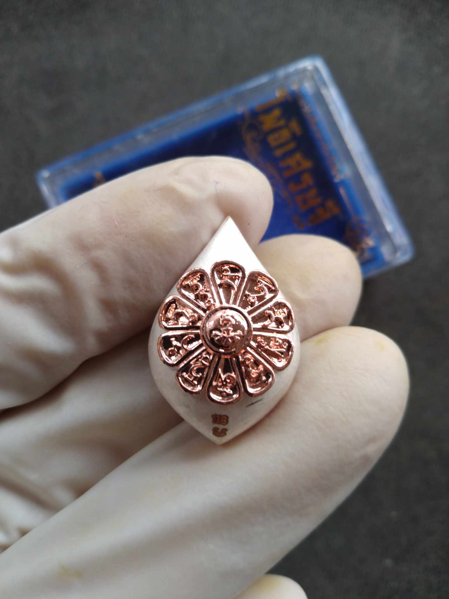 Avalokiteshvara amulet from Thailand teardrop white pendant with copper floral medallion held in gloved hand