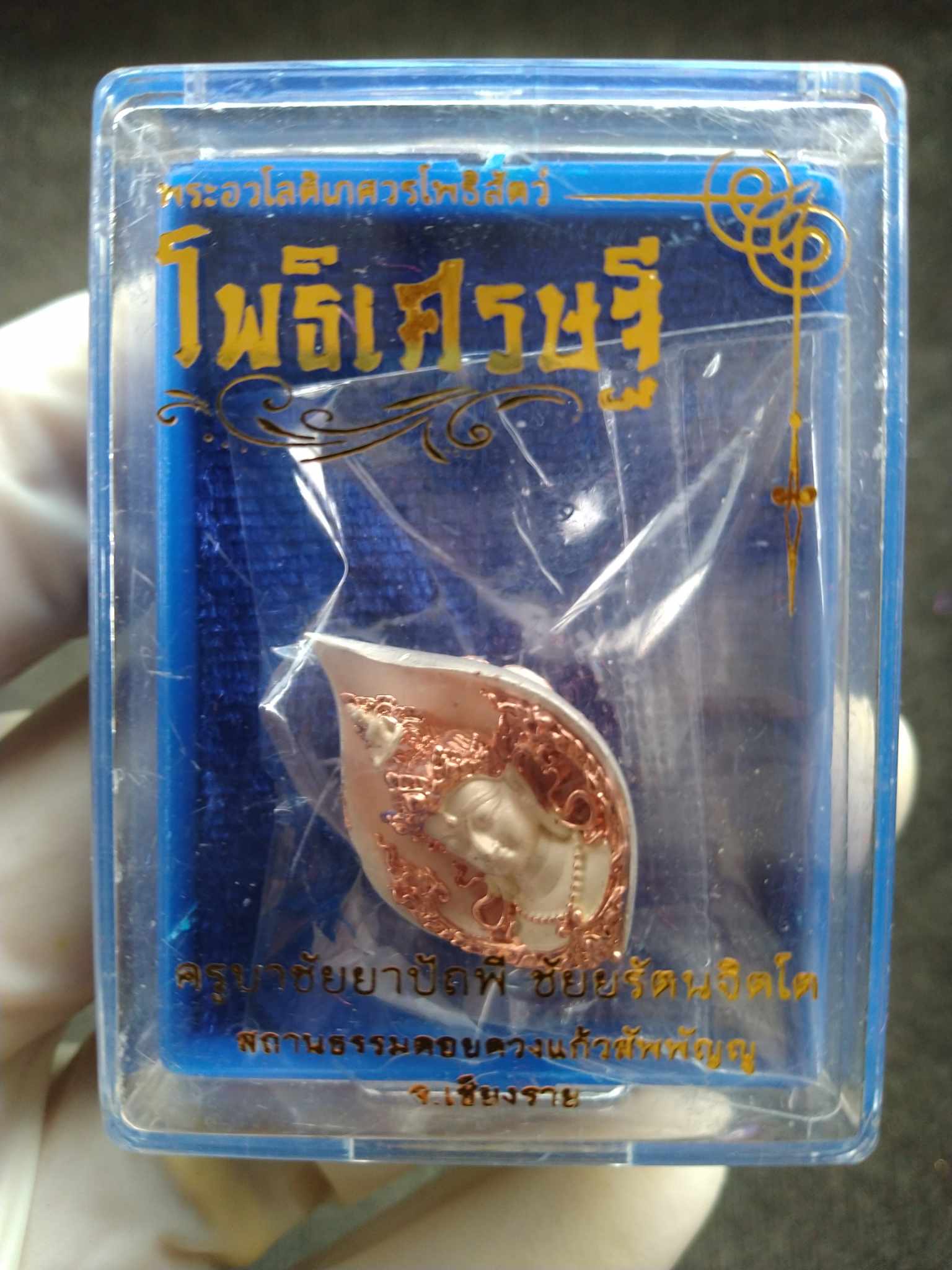 Avalokiteshvara amulet from Thailand in clear blue display case with copper teardrop pendant and Thai script