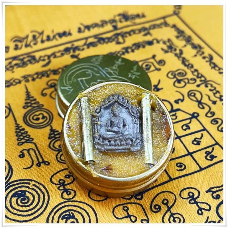 Thai beeswax balm for pain relief in decorative container with intricate design on a fabric background