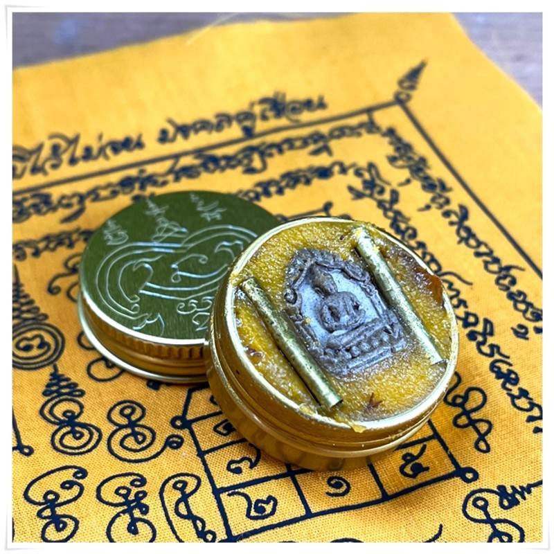 Thai Blessing Co Thai beeswax balm for pain relief in an ornate gold container on a yellow cloth background