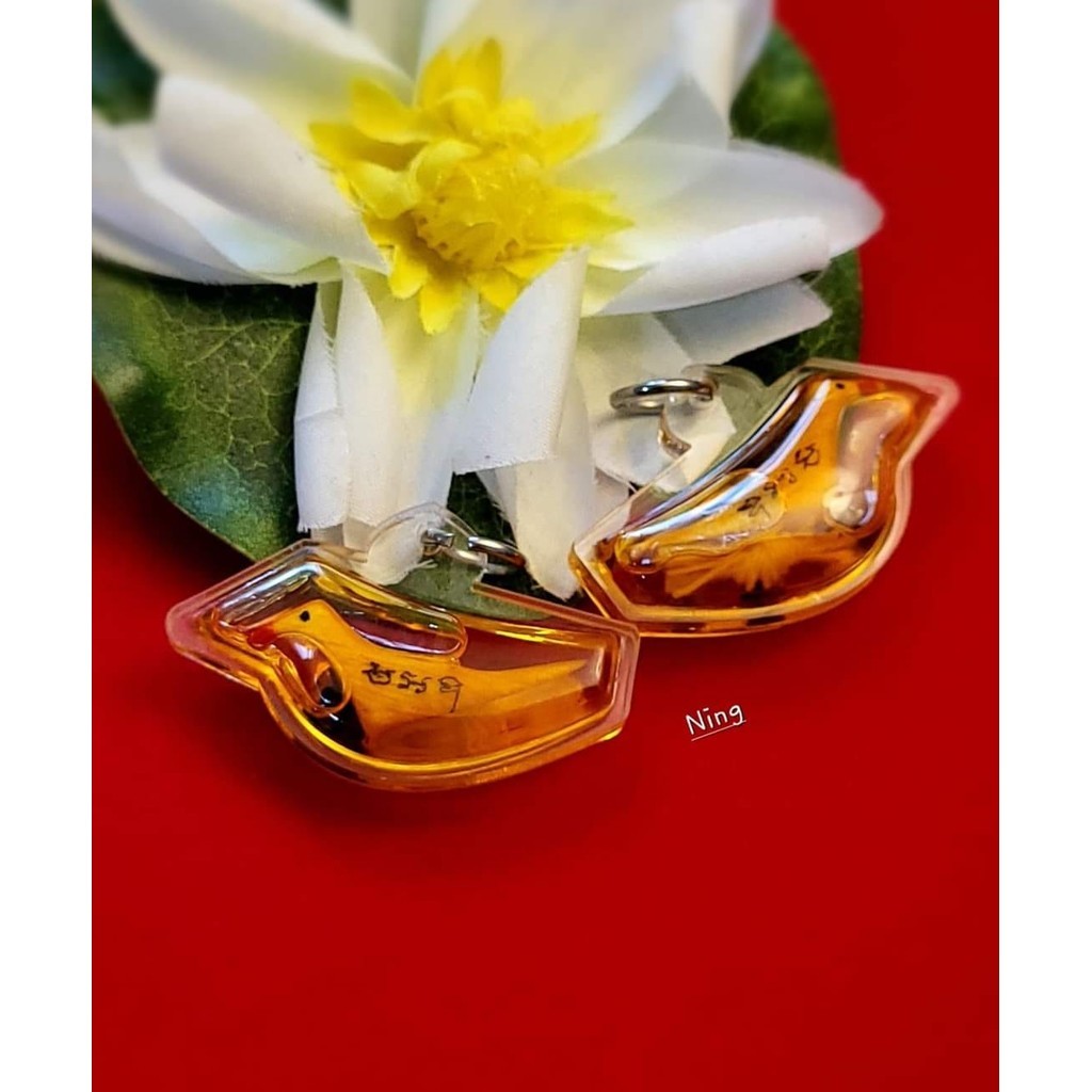 Thai blessed lucky charm bird pendants with amber color casing placed near a white and yellow flower