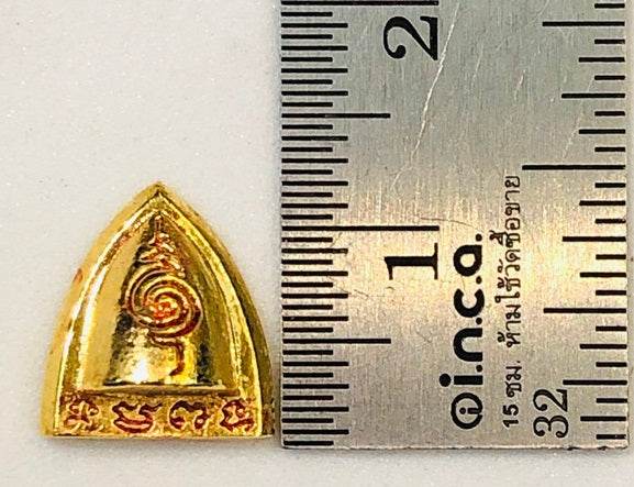 Thai blessed talisman good luck in gold with intricate design next to a ruler for size reference