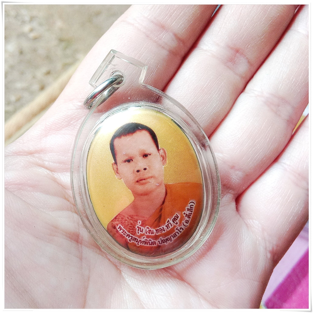Phra Ajarn Tee Lek sacred locket encased in plastic held in hand with a clear photo of the monk