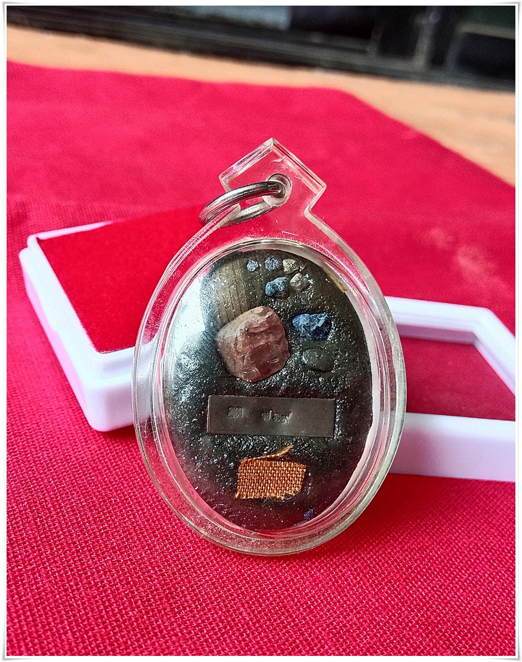Phra Ajarn Tee Lek sacred locket featuring unique materials in a clear protective casing