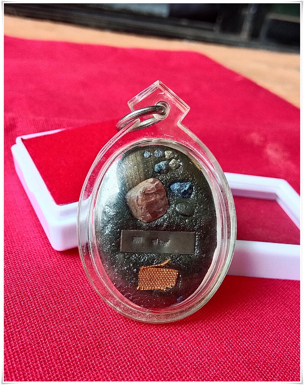 Phra Ajarn Tee Lek sacred locket featuring unique materials in a clear protective casing