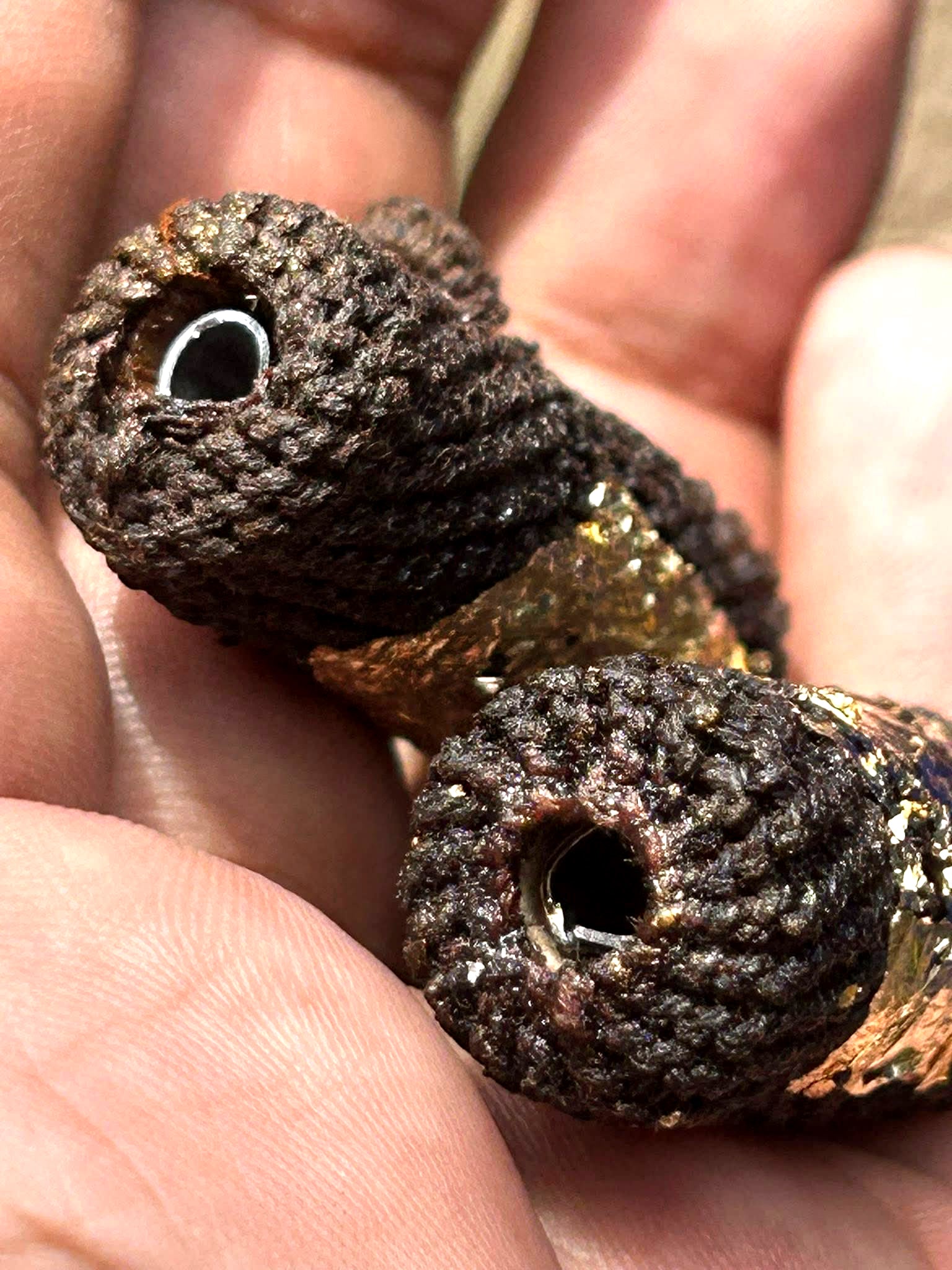 Takrut Phai Tan amulet for protection wrapped in dark brown woven cord with gold leaf accents held in hand