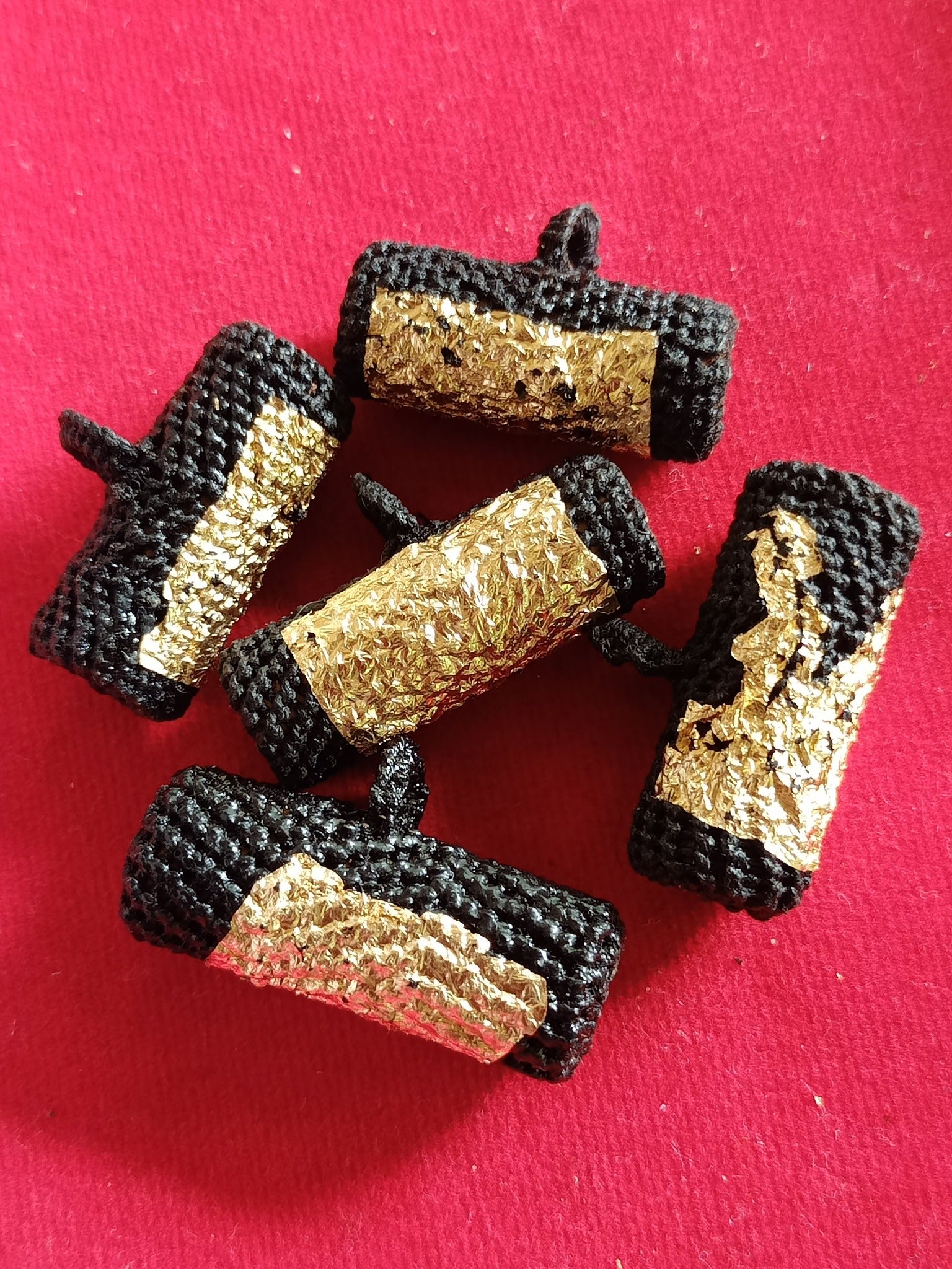 Five black braided Takrut Phai Tan amulet for protection. gold leaf wrapped cylindrical Thai talismans on red cloth