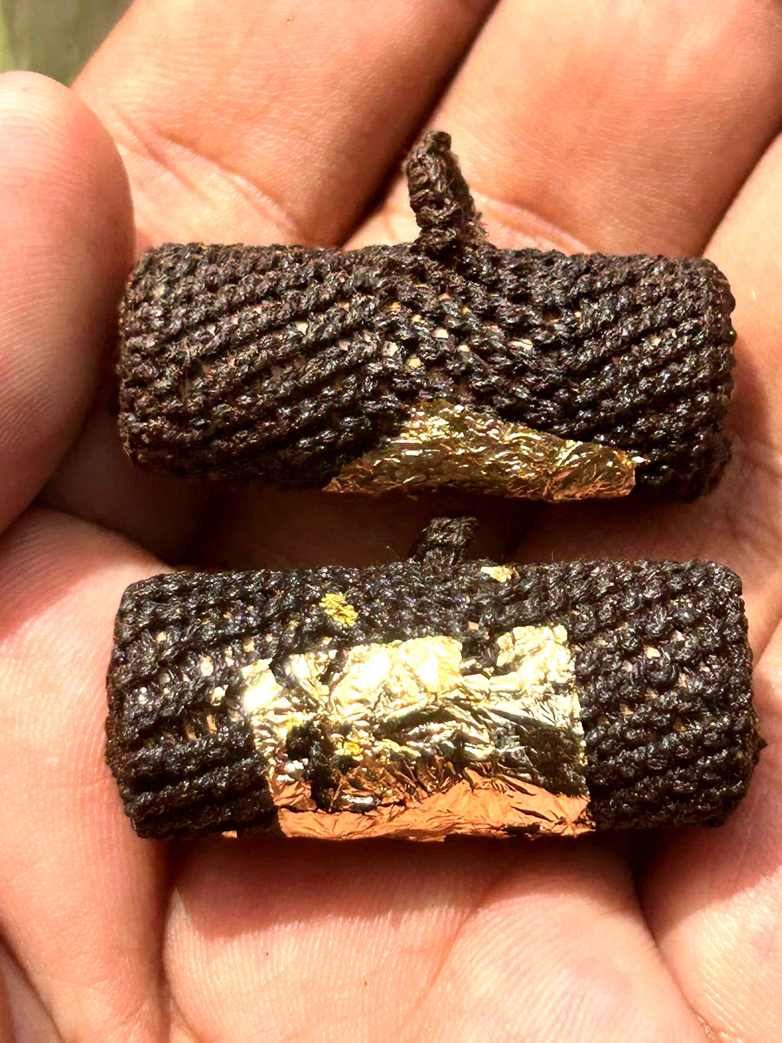 Takrut Phai Tan amulet for protection two black braided takrut tubes with gold foil held in palm