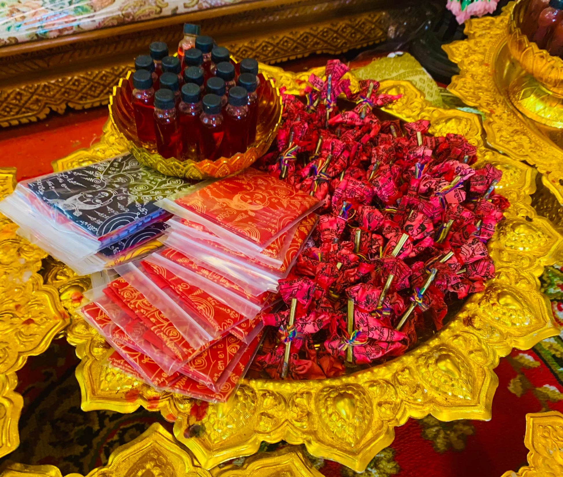 Thai Buddhist charm oil for loving kindness bottles and red wrapped amulets on ornate golden tray