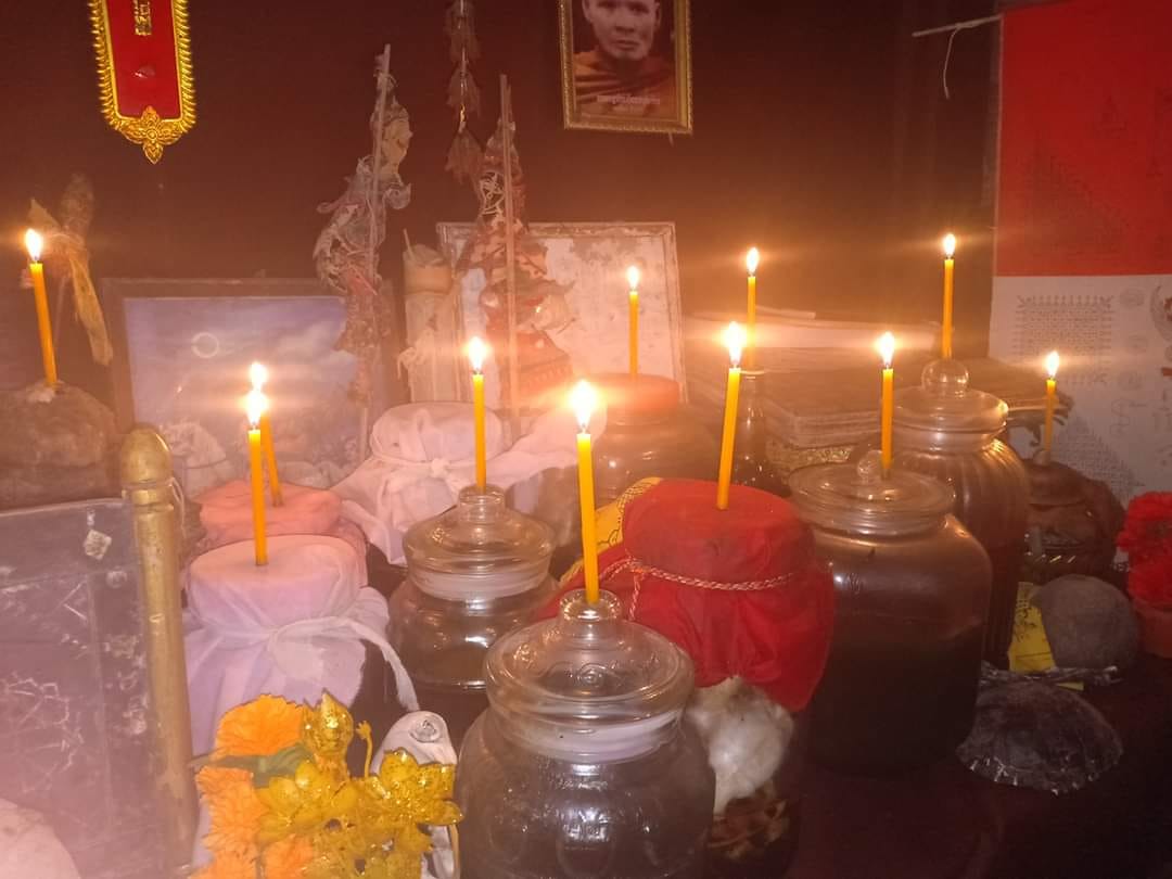 Thai Buddhist charm oil for loving kindness jars on altar with lit yellow candles marigolds and offerings