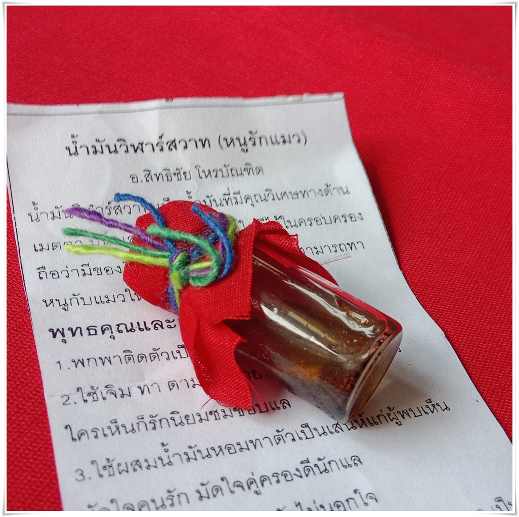 Small glass vial of Thai Buddhist charm oil for loving kindness wrapped in red cloth with multicolor string on Thai paper