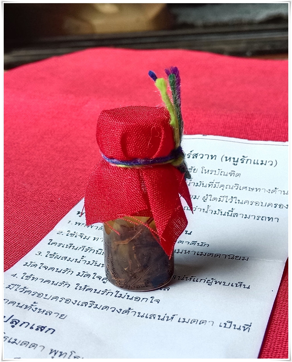 Small glass vial wrapped in red cloth with multicolor string on Thai text paper Thai Buddhist charm oil for loving kindness