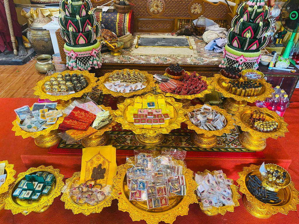 Thai Buddhist charm oil for loving kindness displayed on golden offering trays with amulets and small blessing bottles