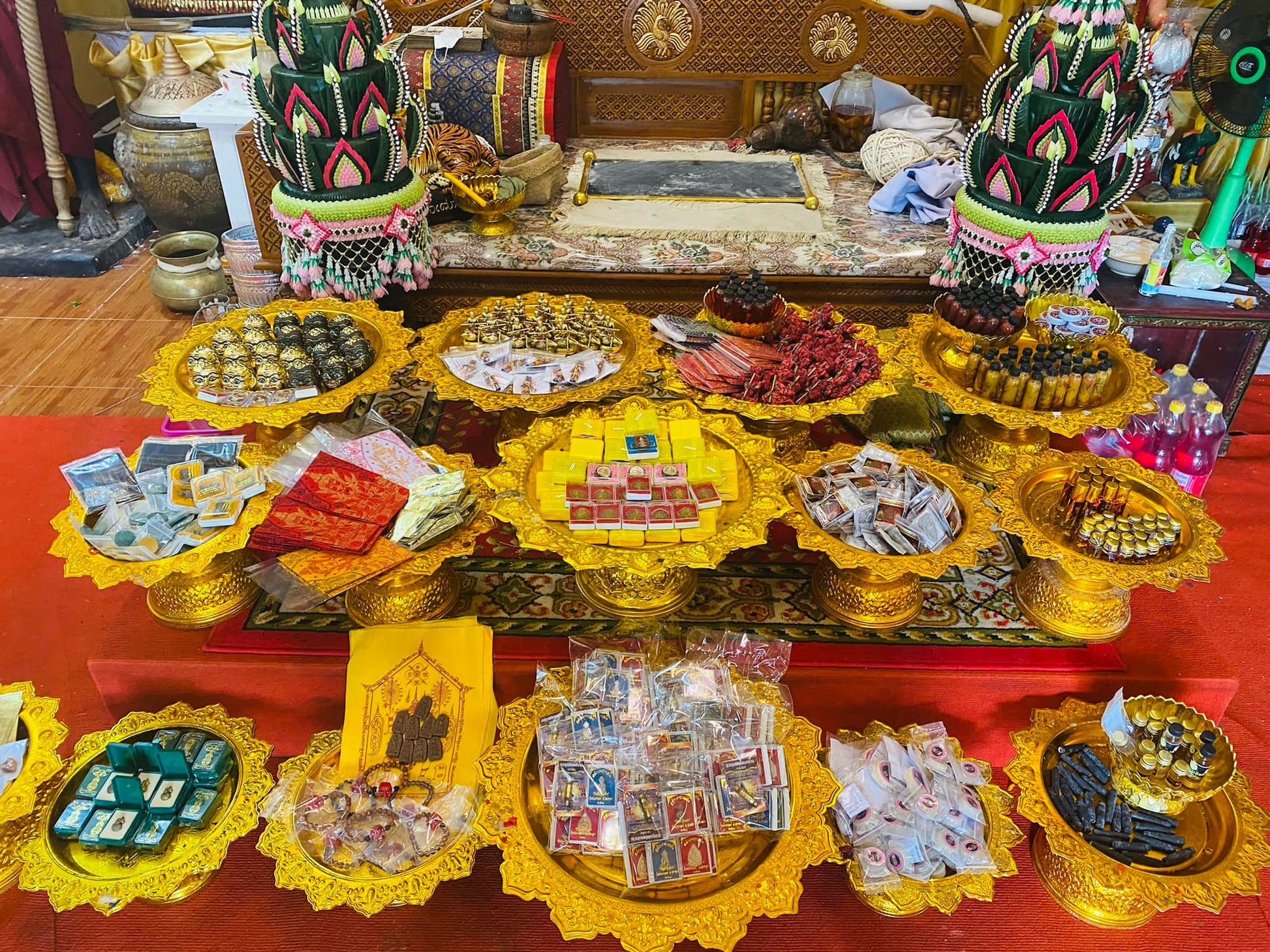 Thai Buddhist charm oil for loving kindness displayed on golden offering trays with amulets and small blessing bottles