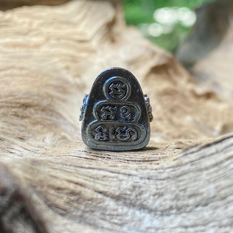 Close-up of blue tone Thai Buddhist amulet with intricate symbols displayed on natural wood surface