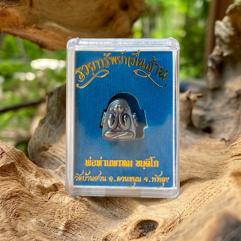 Blue tone Thai Buddhist amulet displayed in a clear plastic case with gold lettering on a wooden surface