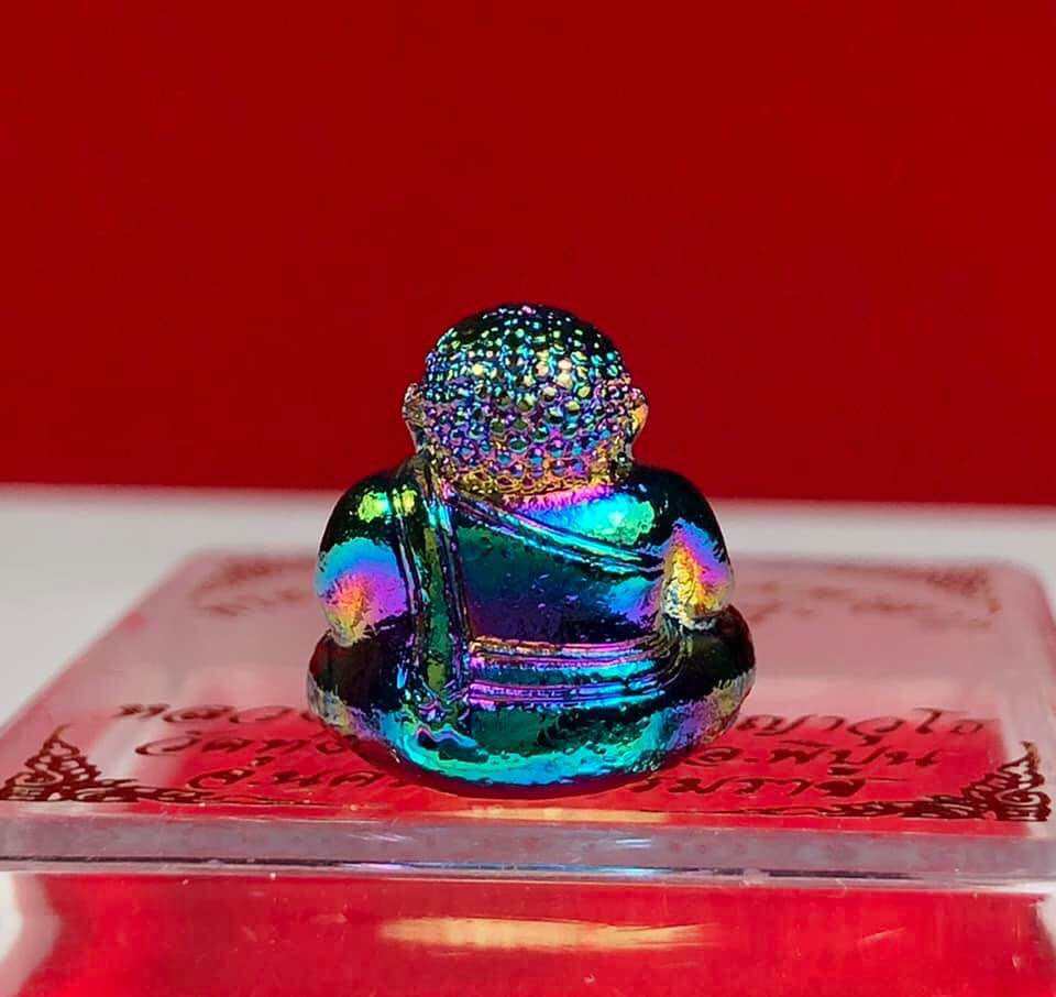Colorful iridescent Thai Buddha debt release amulet figurine placed on a clear display stand