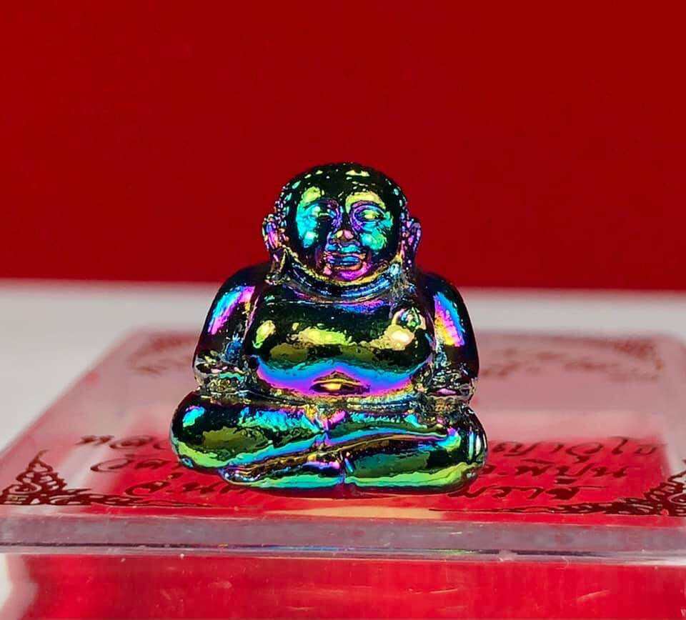 Colorful iridescent Thai Buddha debt release amulet figurine sitting cross-legged on a decorative base