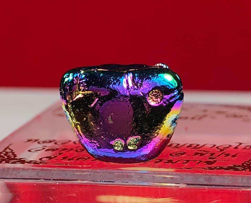 Colorful Thai Buddha debt release amulet with shiny reflective surface on red background