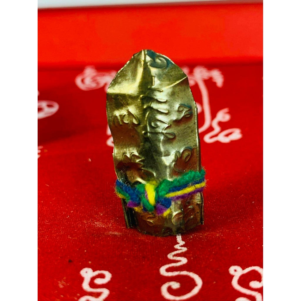 Thai business prosperity amulet with intricate engravings and colorful thread on red fabric background