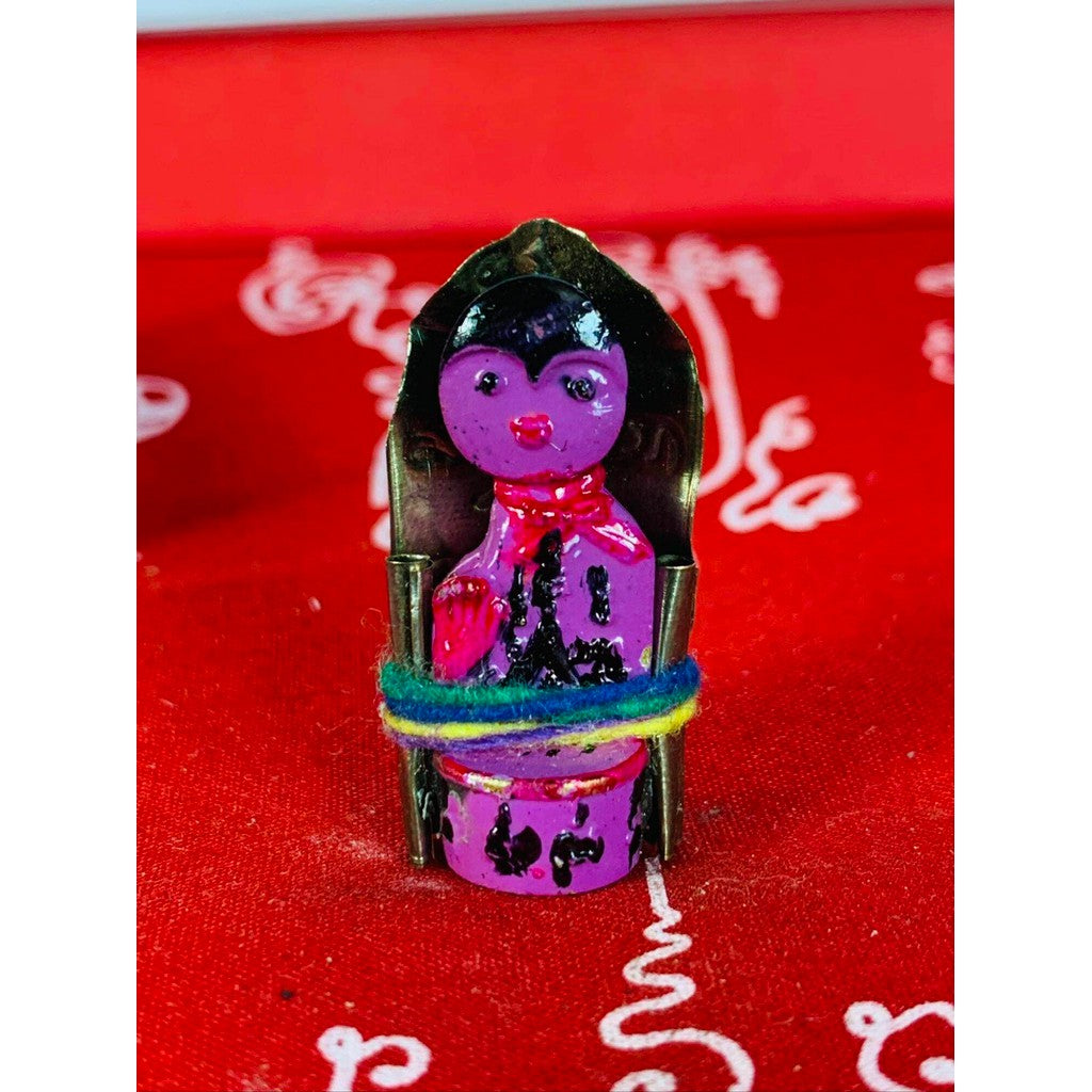 Thai business prosperity amulet with purple figurine wrapped in colorful thread on red fabric background