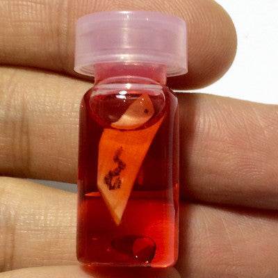 Small bottle of Thai charm oil for luck and popularity, featuring vibrant red liquid and a charm inside