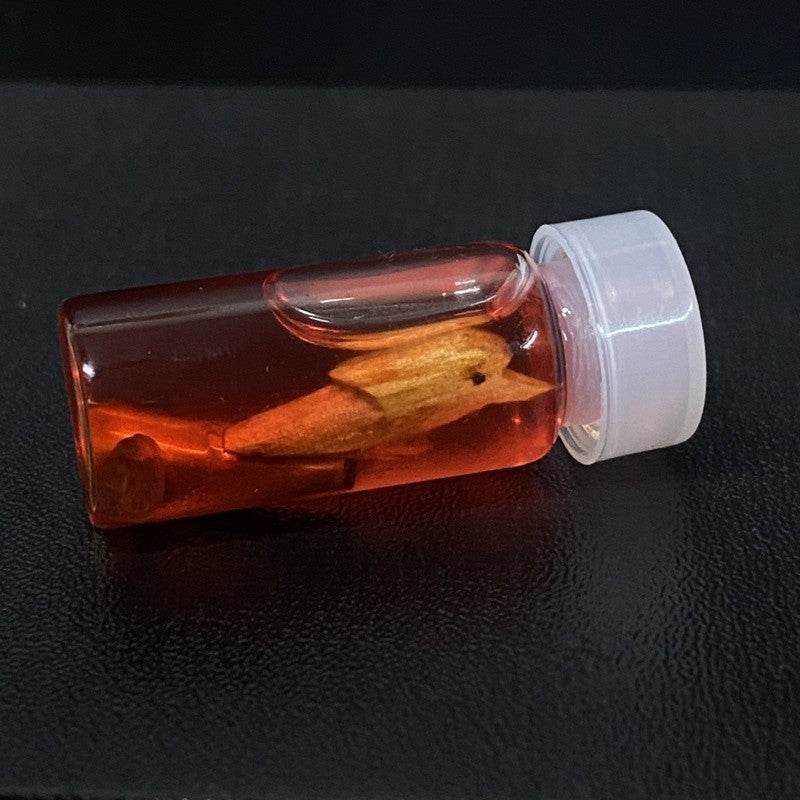 Thai charm oil for luck and popularity in a clear vial with a wooden charm inside