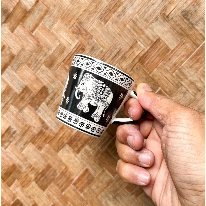 Hand holding a black and white Thai elephant ceramic shot glass with intricate patterns