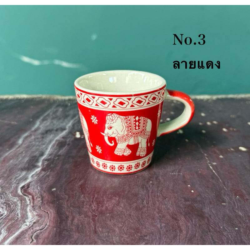 Thai elephant ceramic shot glass with red and white decorative patterns on a textured surface