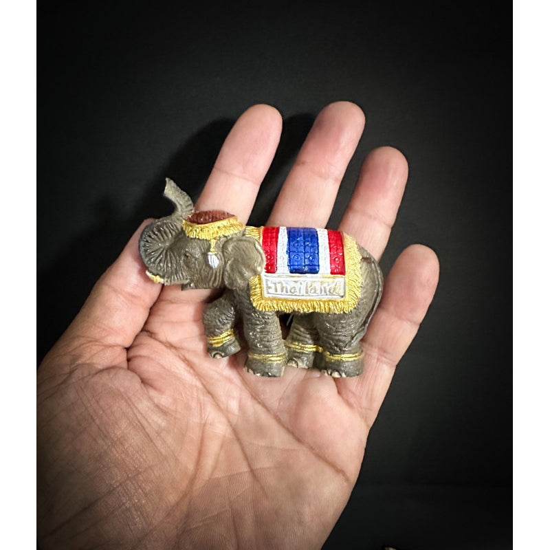 Hand holding a detailed Thai elephant fridge magnet with colorful fabric and Thailand label