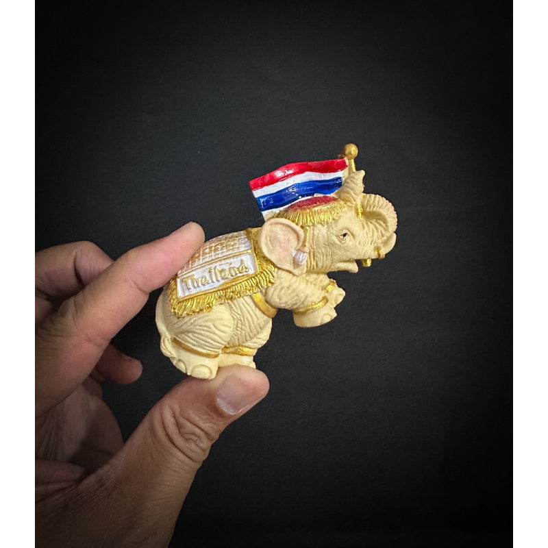 Hand holding a Thai elephant fridge magnet with a small Thai flag and detailed design
