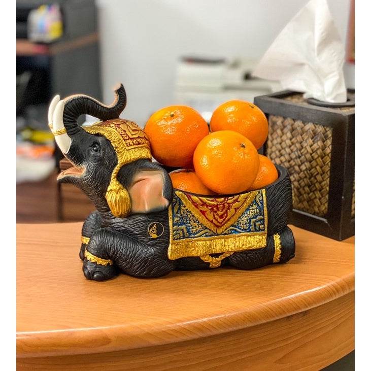 Thai elephant resin tray holding oranges on a wooden table with tissue box nearby
