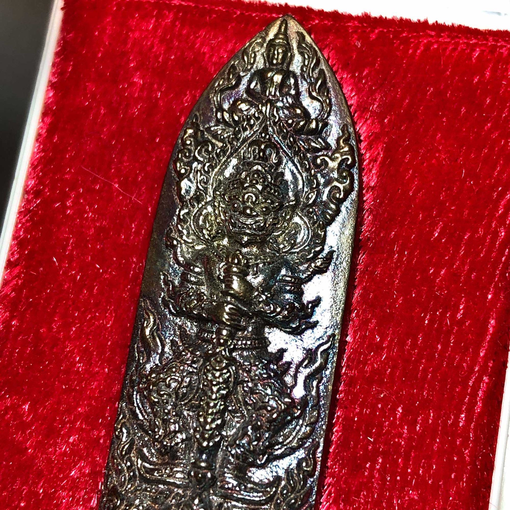 First edition Thao Wessuwan medal dark metal elongated amulet with intricate guardian deity relief on red velvet