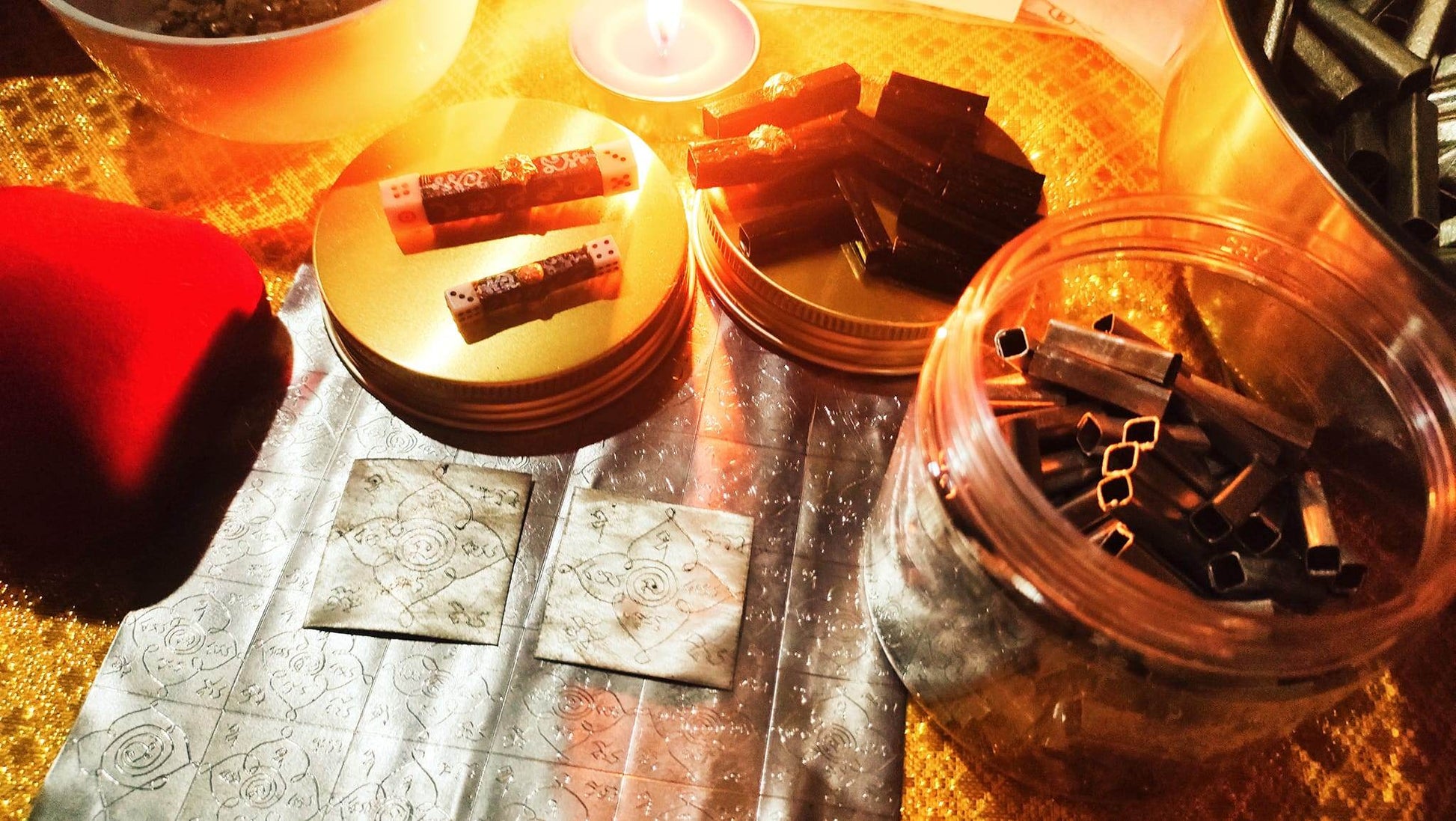 Close-up of Thai gambler's takrud amulet scrolls and metal tubes on a gold cloth under warm candlelight