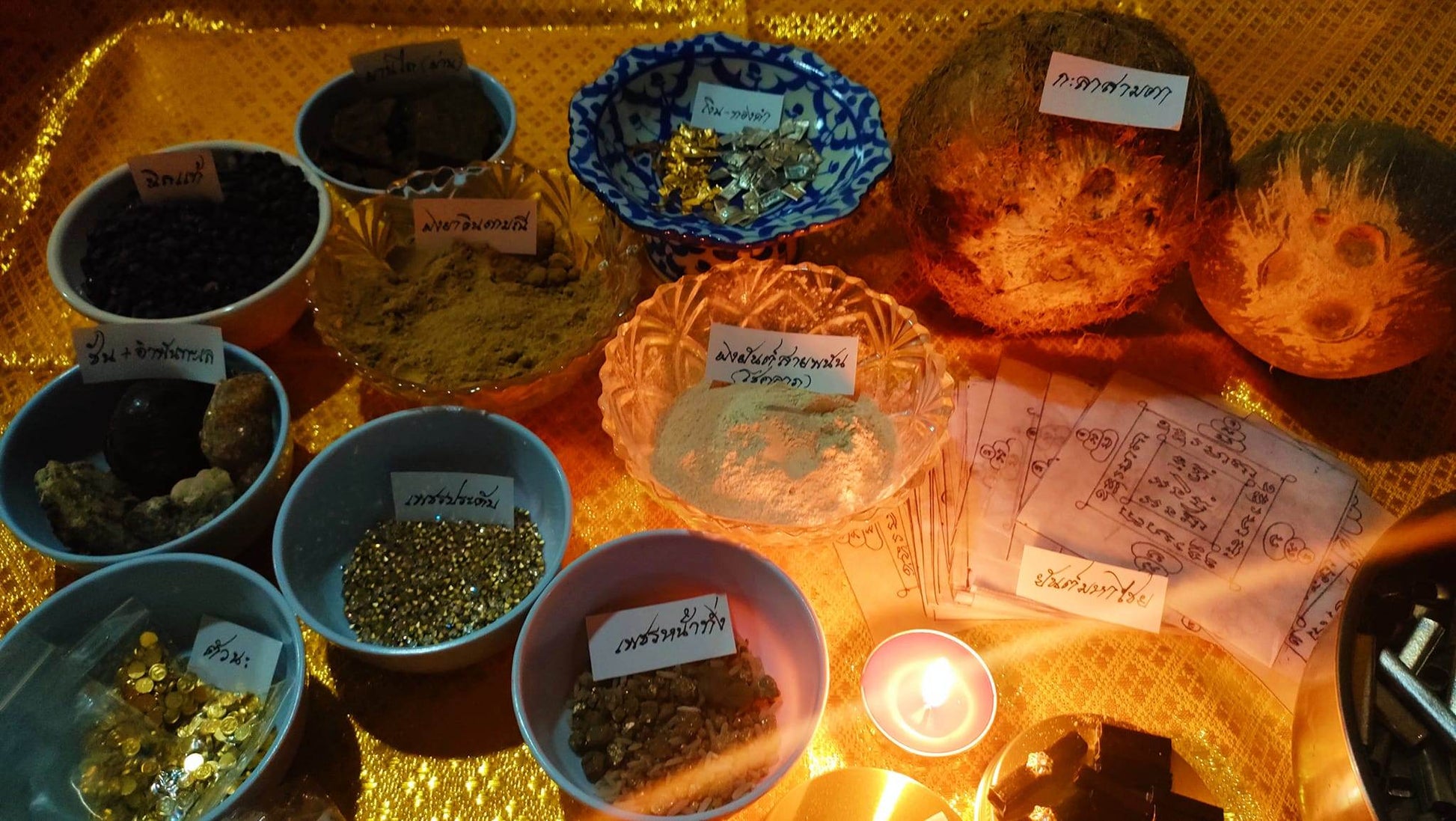 Thai gambler's takrud amulet ritual setup with traditional powders, herbs, gold flakes, and handwritten papers on a woven mat