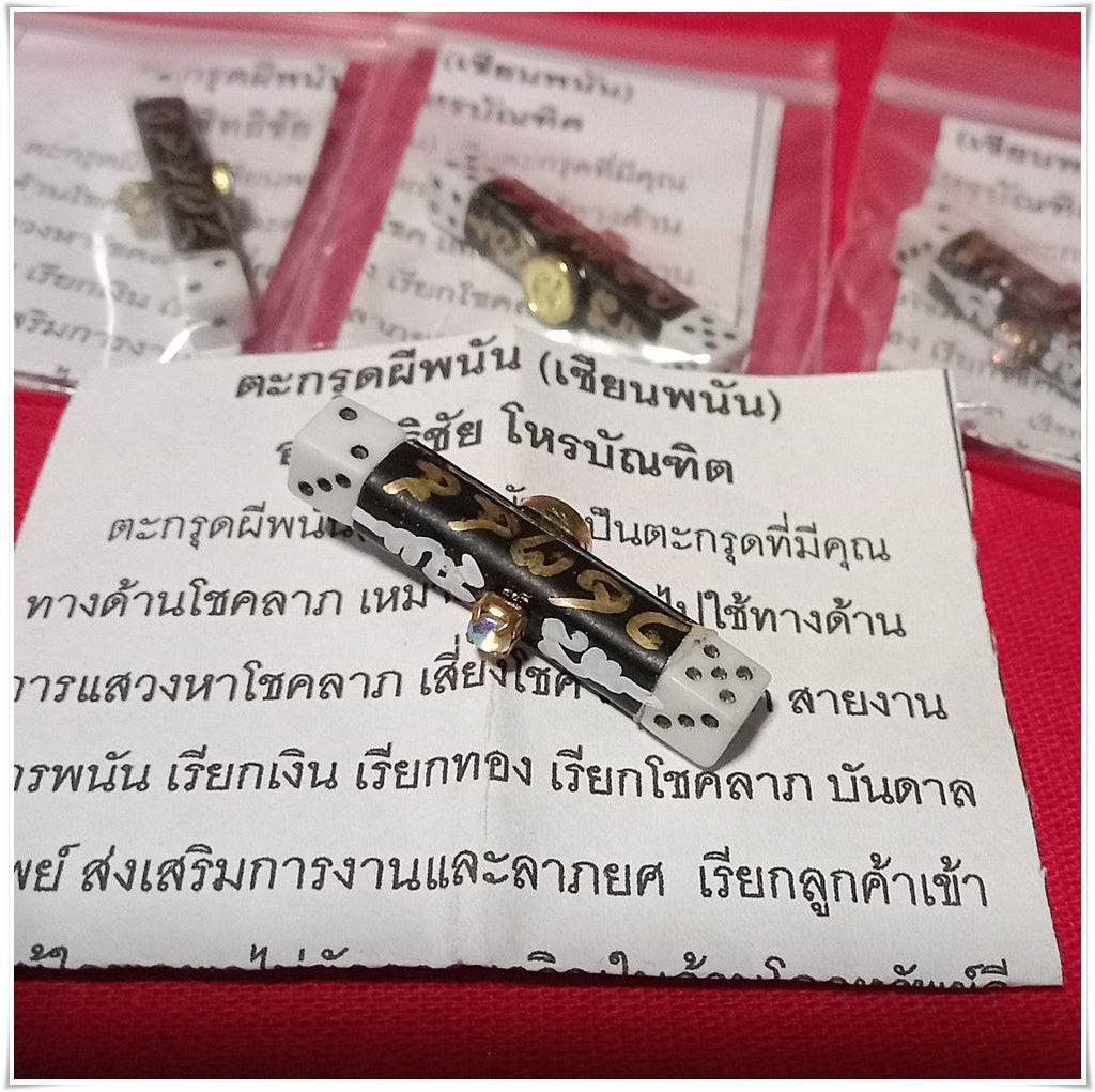 Thai gambler's takrud amulet with intricate gold and white designs displayed on a paper with Thai script