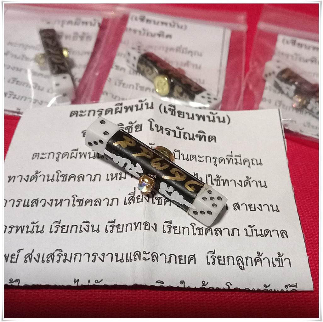 Thai gambler's takrud amulet with black and gold design placed on Thai text paper by Thai Blessing Co