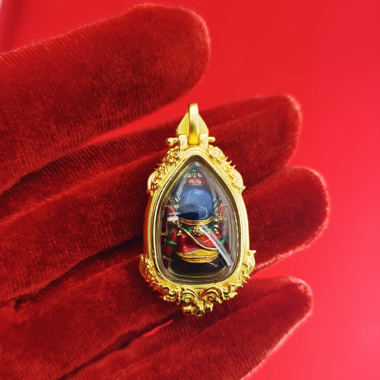 Thai Ganesha pendant for success with intricate details in a gold frame, held in a hand against a red background