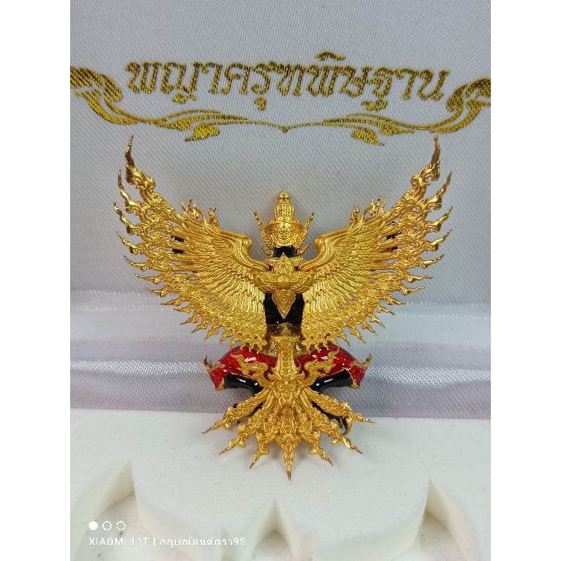 Golden Thai Garuda lucky charm with detailed wings and intricate design on decorative fabric background