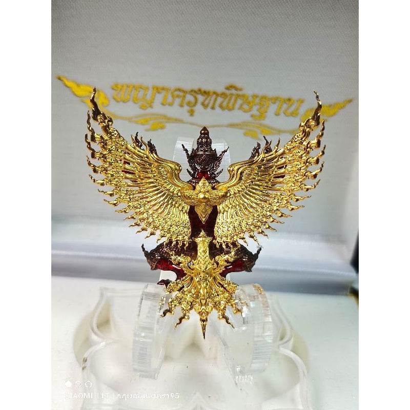 Golden Thai Garuda lucky charm with intricate wing details displayed on a clear stand