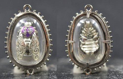 Thai golden bee amulet for wealth with intricate silver detailing and purple accent inside clear protective casing