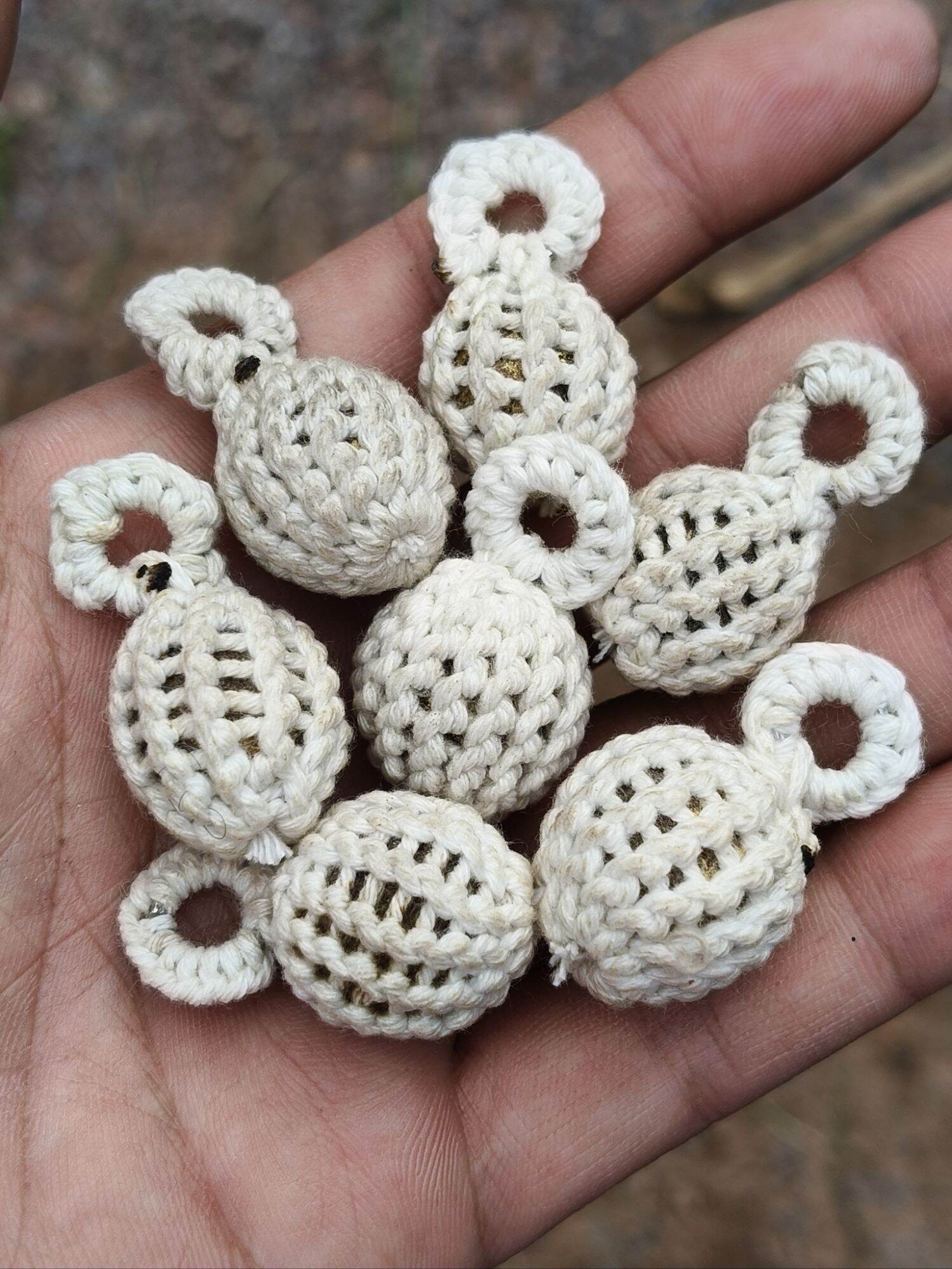Hand holding several cream woven prayer beads with looped tops Jin-Da-Mani magical bead amulet handcrafted by Thai Blessing Co